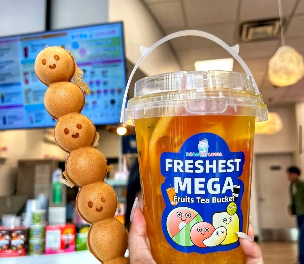 Hand holding mega fruit tea bucket and smiley egg waffle skewer at Boba Cucue.